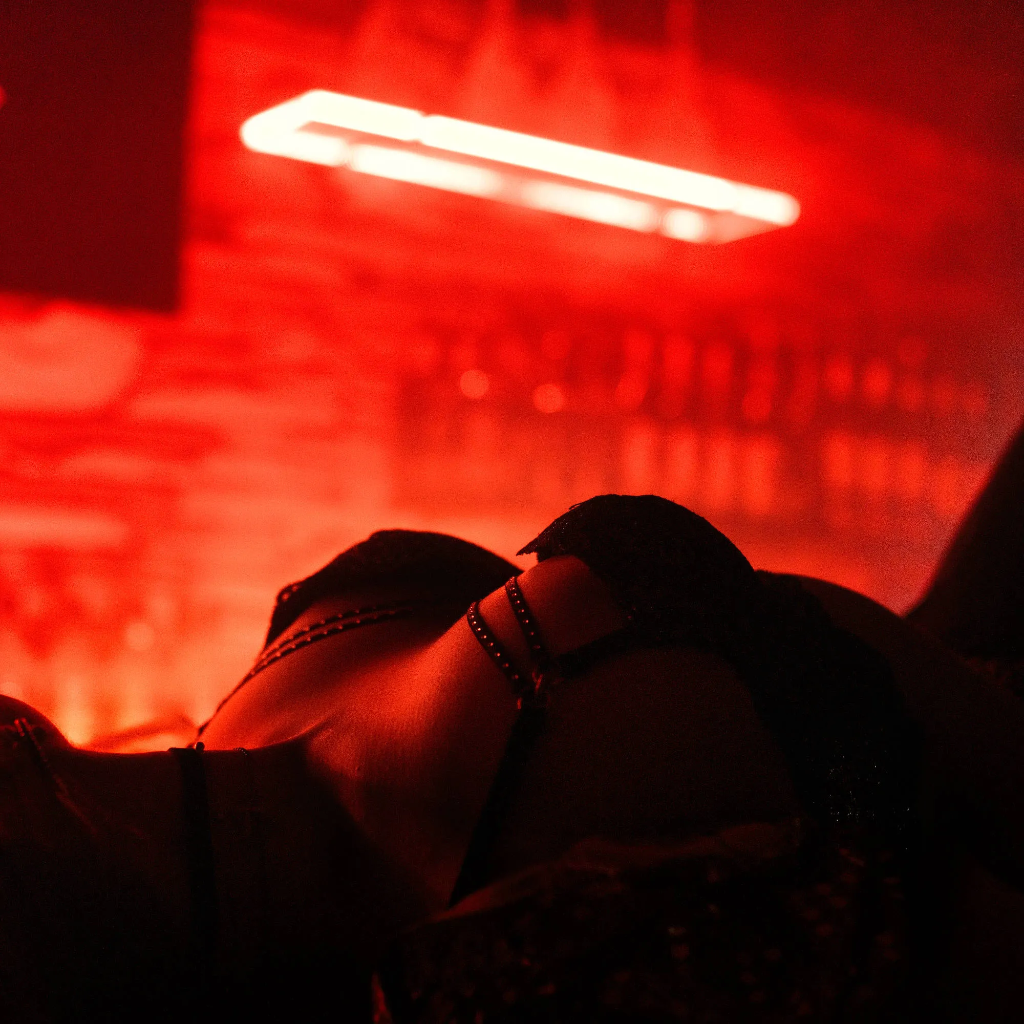 Tanečnice ležící na barovém pultu v tlumeném osvětlení klubu, za ní osvětlené lahve vytvářejí intimní atmosféru prvního kontaktu u baru.